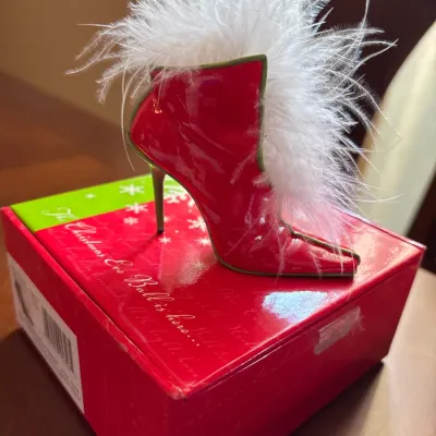 Whimsical red and green miniature high-heeled shoe figurine trim with white feathers, displayed on its original box.