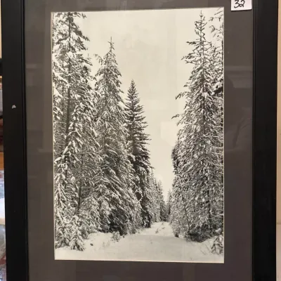 Black and white photographic print depicting a snow-covered forest path, presented in a black mat and matching modern black frame.