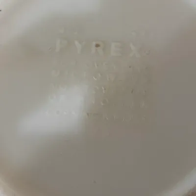 Vintage Pyrex milk glass bowl bottom showing raised maker's mark and oven/microwave safety instructions.
