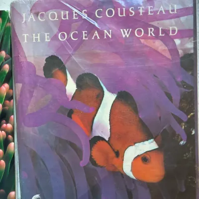 Vintage hardcover copy of "The Ocean World" by Jacques Cousteau, featuring a clownfish and sea anemone on the dust jacket wrapper.