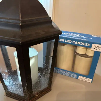 Black metal decorative lantern housing an LED pillar candle, displayed alongside a boxed set of flameless LED candles.