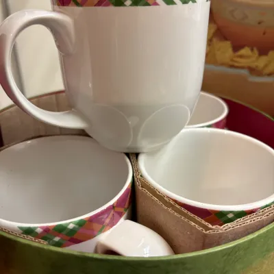 Set of white ceramic coffee mugs featuring a green, pink, and orange plaid rim, stacked inside their original round gift box.