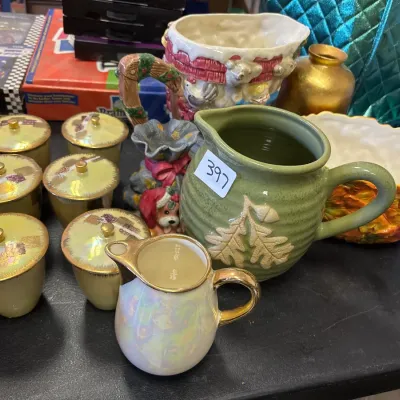 Collection of decorative ceramics and glassware, including an iridescent cream pitcher, lidded spice jars, a sage green ceramic pitcher...