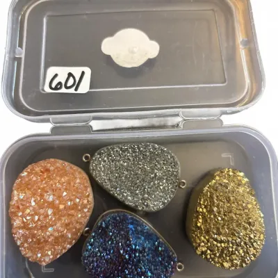 Set of four sparkling teardrop-shaped druzy crystal pendants in metallic tones, organized inside a clear plastic storage container.