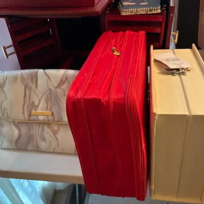 Selection of cosmetic and jewelry organizers, including a marbled soft pouch, a bright red zippered case, and a cream book-style storage...