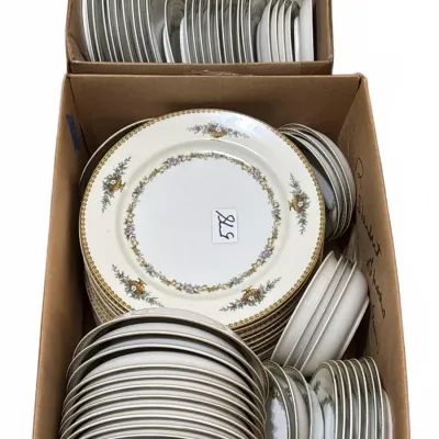 Large vintage porcelain dinnerware service featuring floral garlands, urn motifs, and gold-rimmed borders, packed in cardboard boxes.