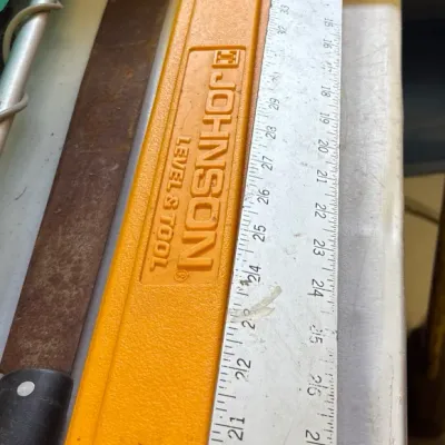 Collection of workshop tools including an orange Johnson level, a long metal ruler, and a rusted hand saw.
