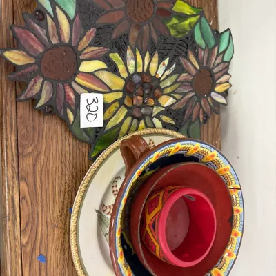 Handcrafted mosaic stained-glass sunflower wall plaque alongside a stack of decorative ceramic bowls and saucers.