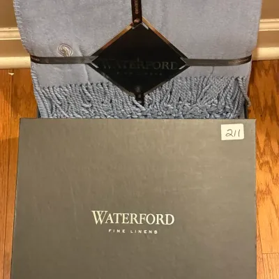 Waterford Fine Linens light blue luxury throw blanket with fringed edges, presented in its original branding box and ribbon packaging.