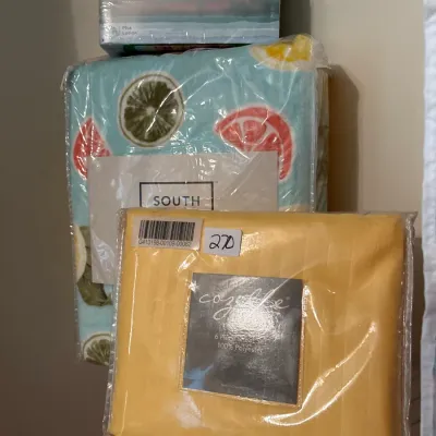 Assortment of packaged household linens, including a Cozelle yellow 6-piece sheet set, a fruit-patterned sheet set by South, and boxes of...