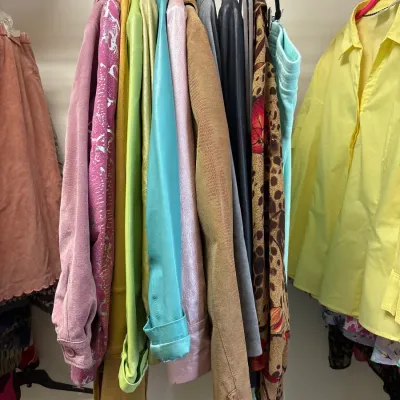 A rack of colorful women's vintage jacket and top options hanging in a closet.