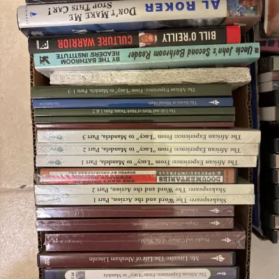Cardboard box packed with assorted hardcovers, paperbacks, and Great Courses educational video sets on DVD.