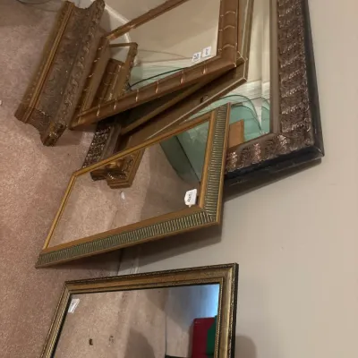 Collection of decorative wall mirrors featuring ornate giltwood, faux-bamboo, and molded metallic frames leaning against a wall.