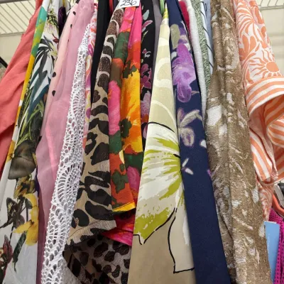 Closet rack packed with colorful women's clothing, featuring bold floral prints, leopard patterns, lace trim, and textured fabrics.