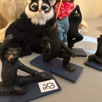 Set of four whimsical black bear yoga pose figurines on dark blue bases alongside a fluffy black and white cat plush.