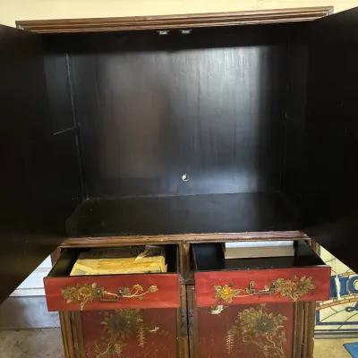 Asian-style hand-painted wooden armoire cabinet featuring floral designs on a red and gold finish, complete with dual upper doors and...