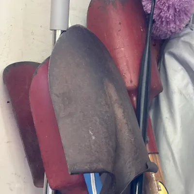 Collection of assorted garden hand shovels, trowels, and household cleaning tools stored together.