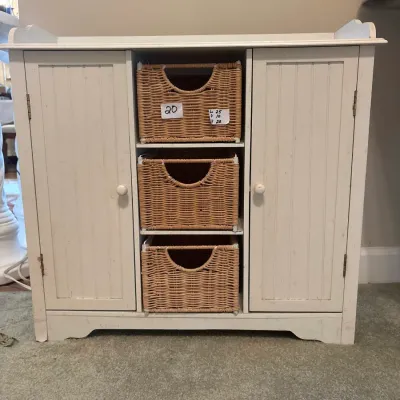 White cottage-style storage cabinet featuring two beadboard side doors and three woven wicker basket drawers.