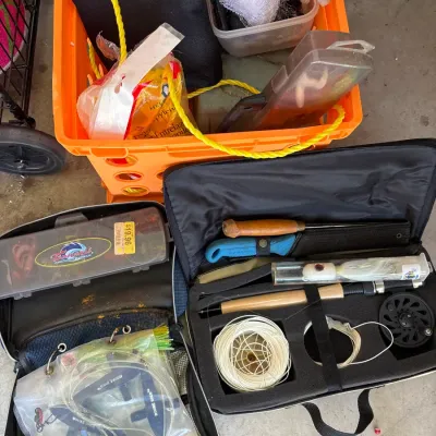 Collection of fishing gear, including a fly fishing rod and reel set in a padded case, tackle boxes, fillet knives, lures, line, and...