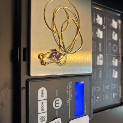 Gold herringbone chain with a square purple stone pendant being weighed on a digital precision scale.