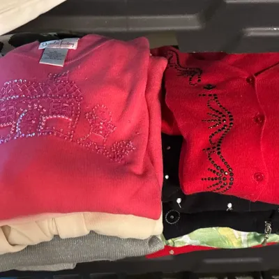 Folded vintage sweaters featuring beaded and embellished designs, including a pink sweater with a gingerbread house motif.