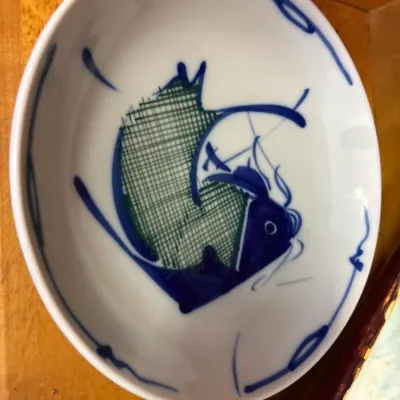 Oval porcelain dish featuring a hand-painted blue and green stylized fish motif with abstract border accents.