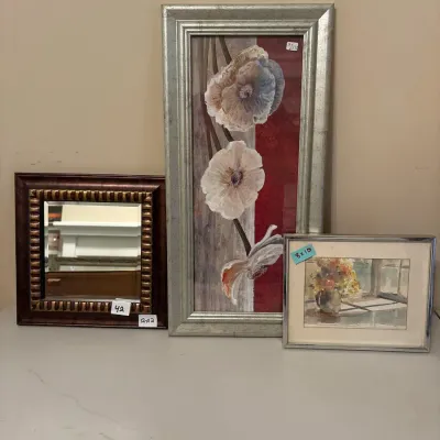 Collection of three framed wall decor items including a small dark wood-framed mirror, a tall silver-framed floral canvas art piece, and...
