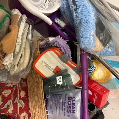 Assorted household cleaning supplies including a purple spin mop bucket, Swiffer products, microfiber cleaning pads, and a woven basket.