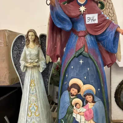 Jim Shore Heartwood Creek angel figurine featuring a nativity scene, displayed alongside a grey and white angel statue.