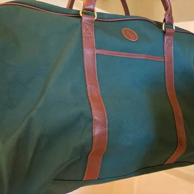 Vintage Polo Ralph Lauren style forest green canvas duffel bag featuring brown faux leather trim, double carry handles, and brass hardware.