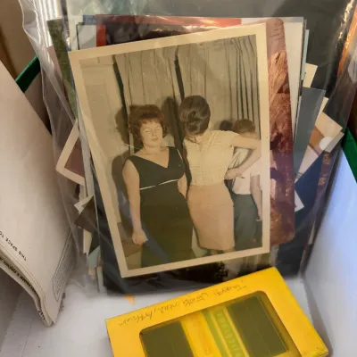 Clear storage bag filled with vintage color photographs from the mid-20th century, accompanied by a yellow box of Fujichrome color slides.