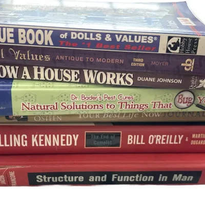 Stack of assorted hardcover and paperback books, including reference guides on dolls, home improvement, and history.