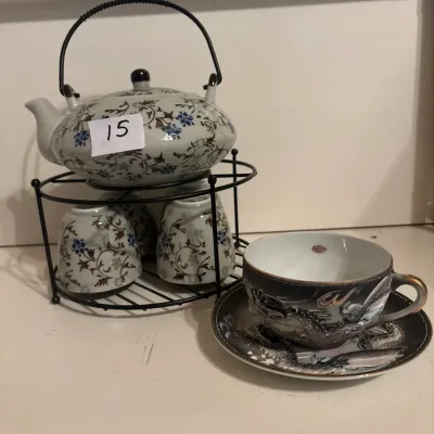 Asian-style floral ceramic teapot set with matching handle-less cups on a metal wire display stand, paired with a detailed dragon-motif...