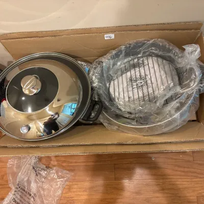 Large wok with a dome lid featuring a built-in thermometer, alongside additional cookware and a wire rack packed in a cardboard box.