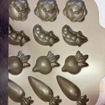 Nordic Ware gold-tone non-stick vegetable patch muffin pan, featuring cabbage, pea pod, radish, and carrot shaped molds.