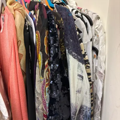 Closet rack packed with colorful women's tops, cardigans, and printed blouses, including sequined and patterned styles.