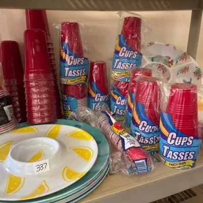 Assortment of plastic party supplies, including stacks of red and yellow disposable cups, small shot cups, and colorful melamine serving...