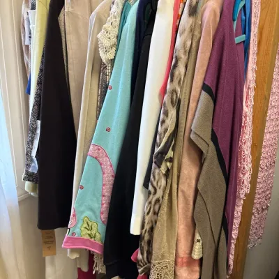 Selection of women's clothing items including cardigans, jackets, and knits, hanging on a closet rack.