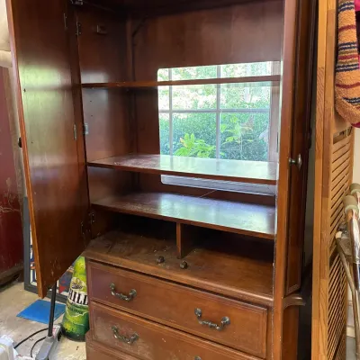 Traditional wooden entertainment armoire with upper cabinet shelving, open back cutout, and two lower drawers with metal bail pulls.