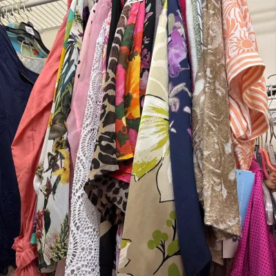 Selection of women's vintage and contemporary clothing hanging on a wire closet rack, featuring a variety of colorful floral prints,...