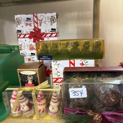 Collection of festive holiday candles and a boxed Hallmark Keepsake Ornament displayed on a wire shelf.