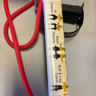 Vintage Tummy Trimmer resistance band exerciser featuring printed instructional diagrams on the handle.