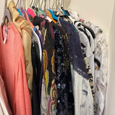 Collection of women's vintage and contemporary clothing hanging on a closet rack, featuring various patterns, sequined tops, and...