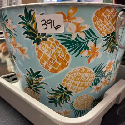 Light blue galvanized metal bucket with a tropical pineapple and floral print, featuring metal side handles.