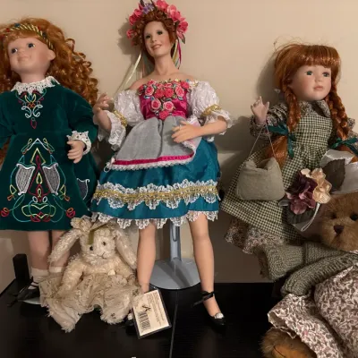 Collection of three red-haired porcelain dolls in detailed folk-style dresses, accompanied by a plush rabbit and a Boyds Bearington...