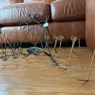 Collection of metal display easels and plate holders in various sizes and finishes, including twisted brass-tone wire and wrought iron...