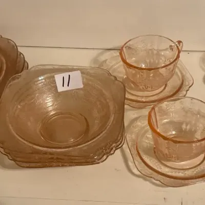 Vintage pink Depression glass tableware set including stacked plates, small bowls, and tea cups with matching saucers.