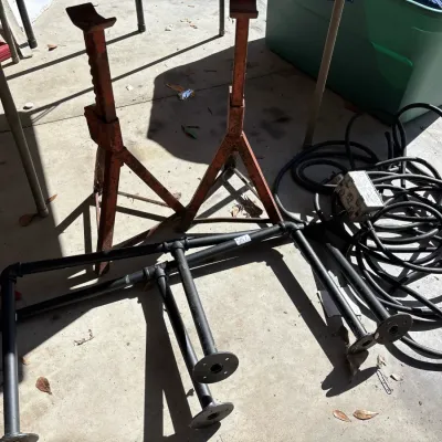Pair of vintage orange jack stands alongside industrial black pipe fittings and a coiled heavy-duty extension cord on a garage floor.