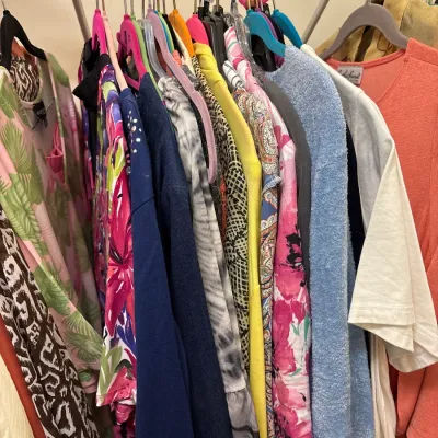 Selection of women's vintage and contemporary clothing, featuring colorful prints, knits, and tops, hanging on a metal rack.
