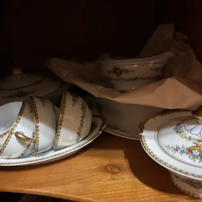 Vintage fine china dining set featuring floral garlands and gilt trim, including teacups, serving platters, a gravy boat, and covered...